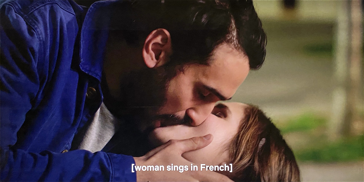 A man is passionately kissing a woman and the subtitles say WOMAN SINGS IN FRENCH.