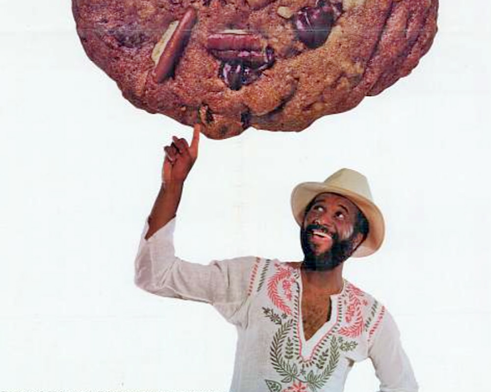 Famous Amos holding up a giant cookie with one finger!