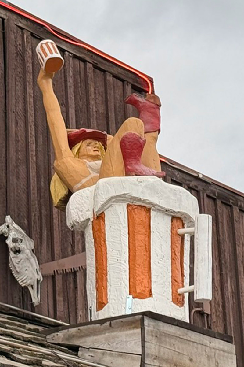 A wooden sculpture of a cowgirl in a giant beer mug holding a beer mug!