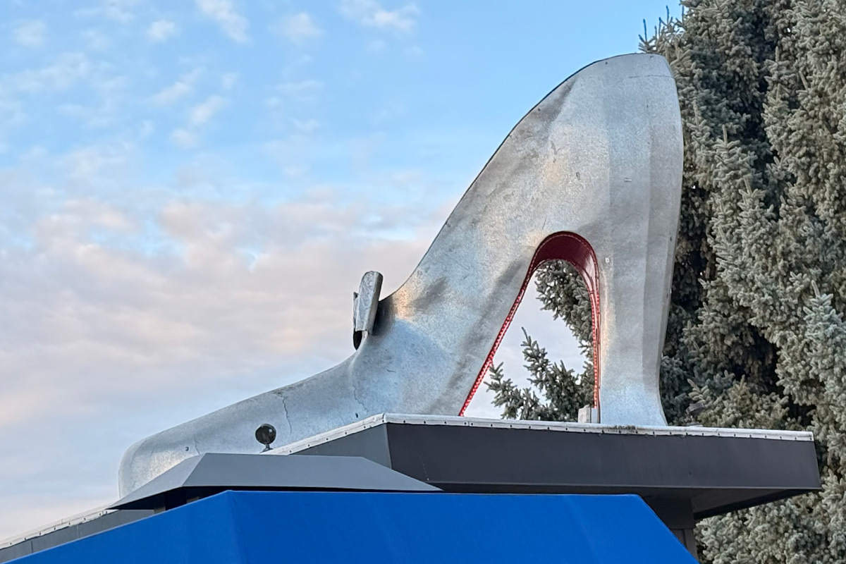 A giant silver high-heel shoe sculpture on top of a small building.