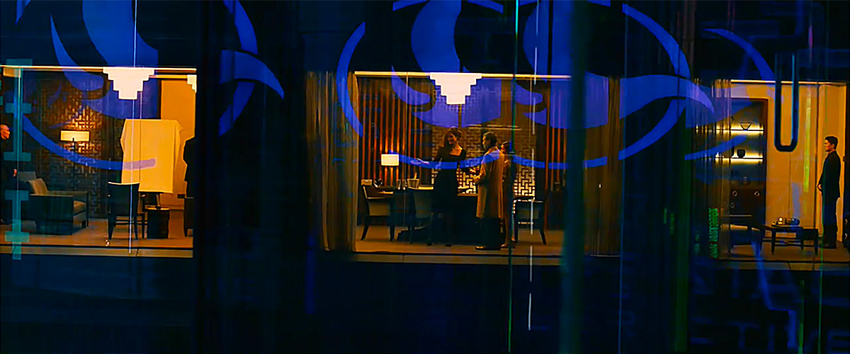 James Bond out to get an assassin with colorful lights and images reflecting on glass walls.